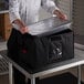 A chef using a Cambro Jumbo Delivery GoBag to hold a large metal container on a table.