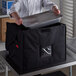 A chef putting a metal container in a black Cambro Delivery GoBag.