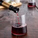 A bottle pouring red liquid into a glass with a Franmara Twist-Pour Black Wine Stopper/Pourer.