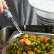 A hand using a Vollrath spoodle to serve vegetables from a pan.