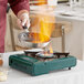 A chef cooks food in a pan on a green Choice Green portable gas stove with a flame.