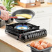 A person cooking an omelette on a Sterno butane countertop stove with blue flames.
