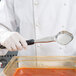 A person using a Vollrath Jacob's Pride black solid oval spoodle to serve red sauce.
