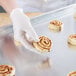 A person in gloves putting cinnamon rolls on a Chicago Metallic wire in rim aluminum sheet pan.