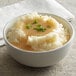 A bowl of mashed potatoes with green onions and gravy.
