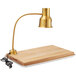 An Avantco gold heat lamp on a wooden cutting board.