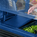 A hand opens a navy blue Cambro Versa well cover to reveal a tray of greens.