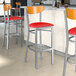 A group of Lancaster Table & Seating bar stools with red vinyl seats and cherry wood backs.