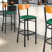 A Lancaster Table & Seating Boomerang series bar stool with a green vinyl seat and cherry wood back.