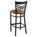 A Lancaster Table & Seating black cross back bar stool with a light brown cushioned seat.