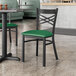 A black Lancaster Table & Seating cross back chair with a green vinyl padded seat at a table in a restaurant.