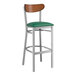 A Lancaster Table & Seating bar stool with a green vinyl seat and antique walnut wood back.