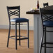 A Lancaster Table & Seating black cross back bar stool with a navy blue cushion next to a table.