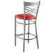 A Lancaster Table & Seating clear coat finished metal cross back bar stool with a red vinyl cushion.