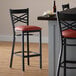 A Lancaster Table & Seating black cross back bar stool with burgundy vinyl seat.