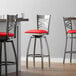 A close up of a Lancaster Table & Seating clear coat finish cross back swivel bar stool with a red vinyl padded seat.