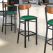 Three Lancaster Table & Seating Boomerang Series bar stools with green vinyl seats and antique walnut wood backs.