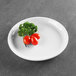 A white Elite Global Solutions round melamine coupe plate with cherry tomatoes and parsley on it.