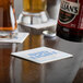 A beer bottle being poured into a customizable paper coaster on a table.