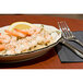 A CAC ivory china platter with a scalloped edge and black band holding shrimp and rice with lemon wedges and a fork.