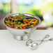 A silver bowl of salad with a pair of Tabletop Classics by Walco stainless steel salad tongs.
