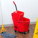 A Rubbermaid red mop bucket with a red dirty water bucket attached to it on a wood floor.