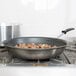 A Vollrath stainless steel frying pan with food cooking on a stove.