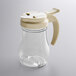 A clear polycarbonate teardrop syrup server with a tan almond top.