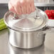 A hand using a Vollrath stainless steel pot lid to cover a pot.