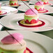 A group of RAK Porcelain ivory porcelain flat plates of desserts with a pink and green dessert on top.
