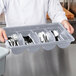 A chef holding a Cambro polyethylene container with silverware in it.