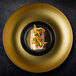 A RAK Porcelain gold and black porcelain plate with food on it.