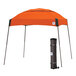 An orange E-Z Up canopy with a steel gray frame and a roller bag.