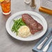 A Acopa narrow rim stoneware plate with steak, mashed potatoes, and green beans on a table.
