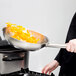 A person cooking food in a Vigor stainless steel frying pan.
