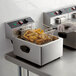 A hand in gloves uses a Galaxy fryer basket to prepare french fries in a commercial fryer.