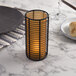 An orange frosted Sterno table lamp on a table with a candle and bread plates and glasses.