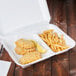 A white Genpak foam container with fried fish and chicken with lemon wedges.