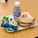A white Genpak foam school tray with a sandwich, chips, and a white cup on it.
