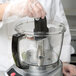 A person in gloves using a Waring food processor on a counter.