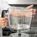 A person holding a clear container on the counter in a professional kitchen.