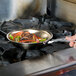 A person cooking food in a Vollrath stainless steel frying pan on a stove.