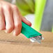 A hand holding a Pacific Handy Cutter green right-hand safety knife cutting a box.