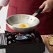 A person using a Choice aluminum fry pan to cook a fried egg on a gas stove.