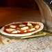 A GI Metal square perforated pizza peel with a pizza cooking in a wood fired oven.