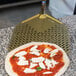 A GI Metal square perforated pizza peel with a pizza topped with cheese and basil on it.