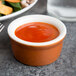 A Tuxton Autumn white china ramekin filled with red sauce on a table next to food.