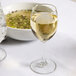 A Libbey tall wine glass filled with white wine on a table next to a bowl of soup.