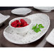 A white Elite Global Solutions round melamine bowl filled with raspberries.