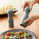 A person using an Acopa wooden blue pepper mill to season a salad.